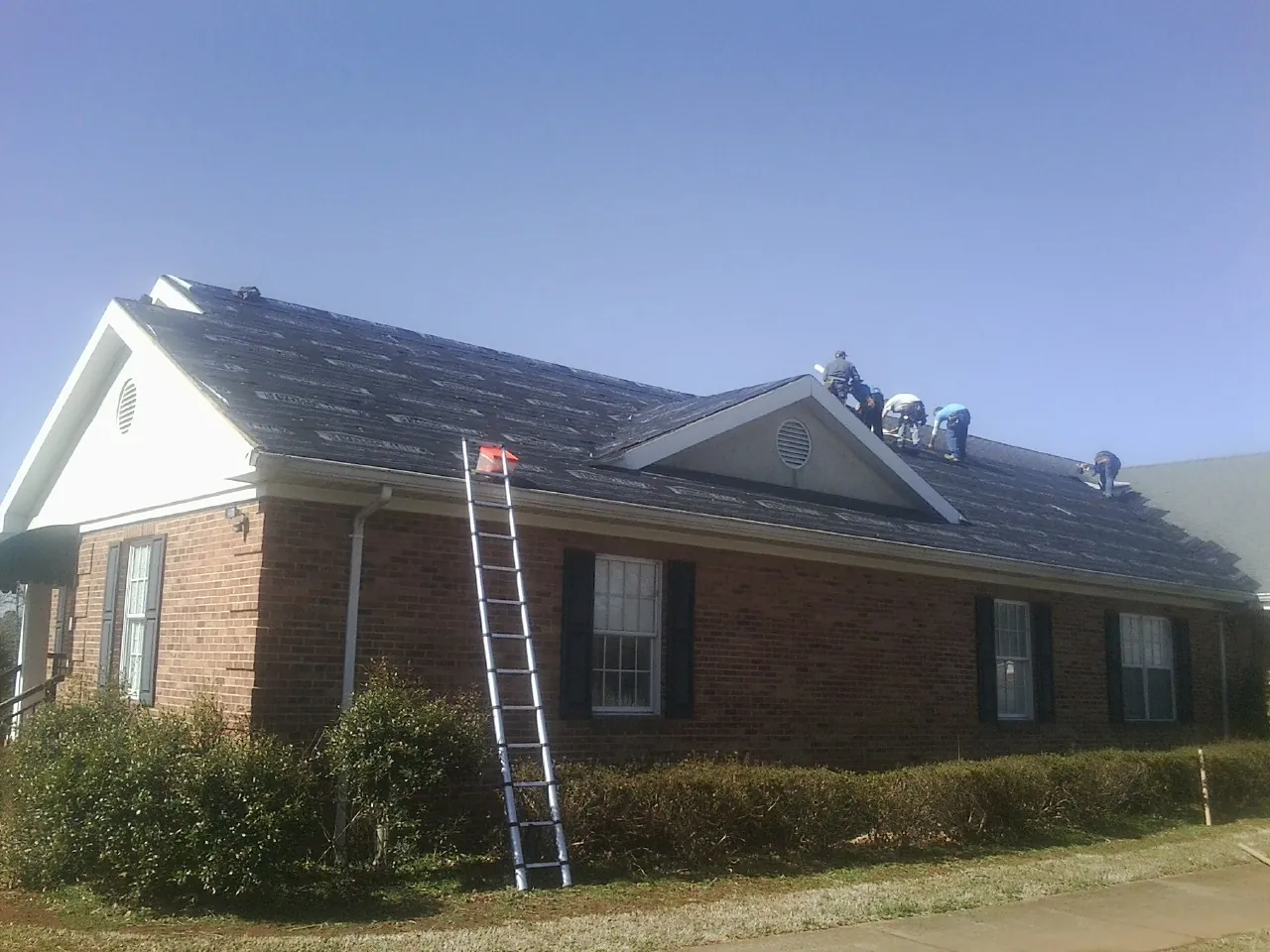Crew tearing shingles off a brick ranch roof with a ladder set — Emergency Roof Repair work by our crew in Carleton