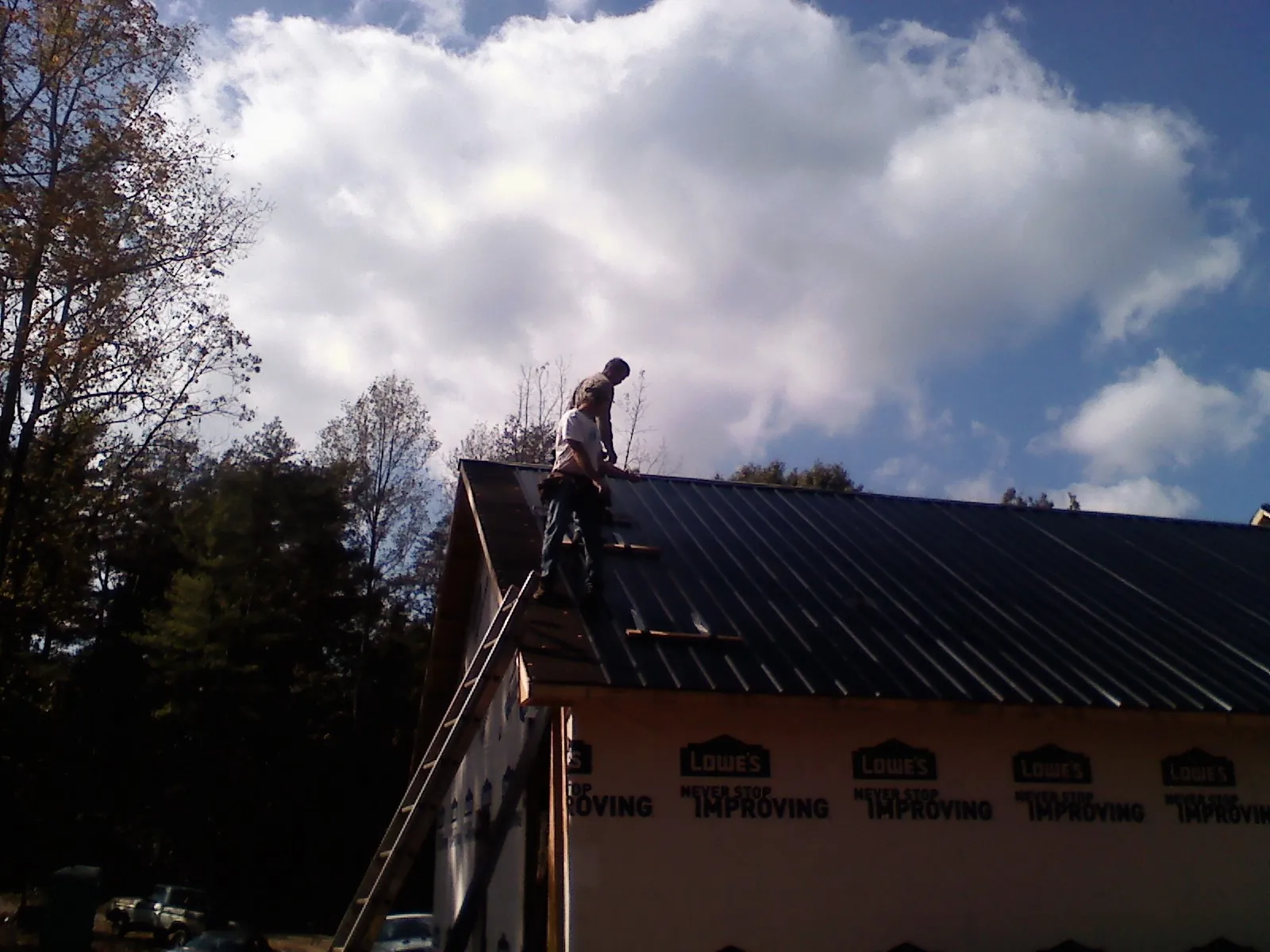 Roofer fastening dark metal panels high against a cloudy sky, from a Roof Inspection job in Carleton