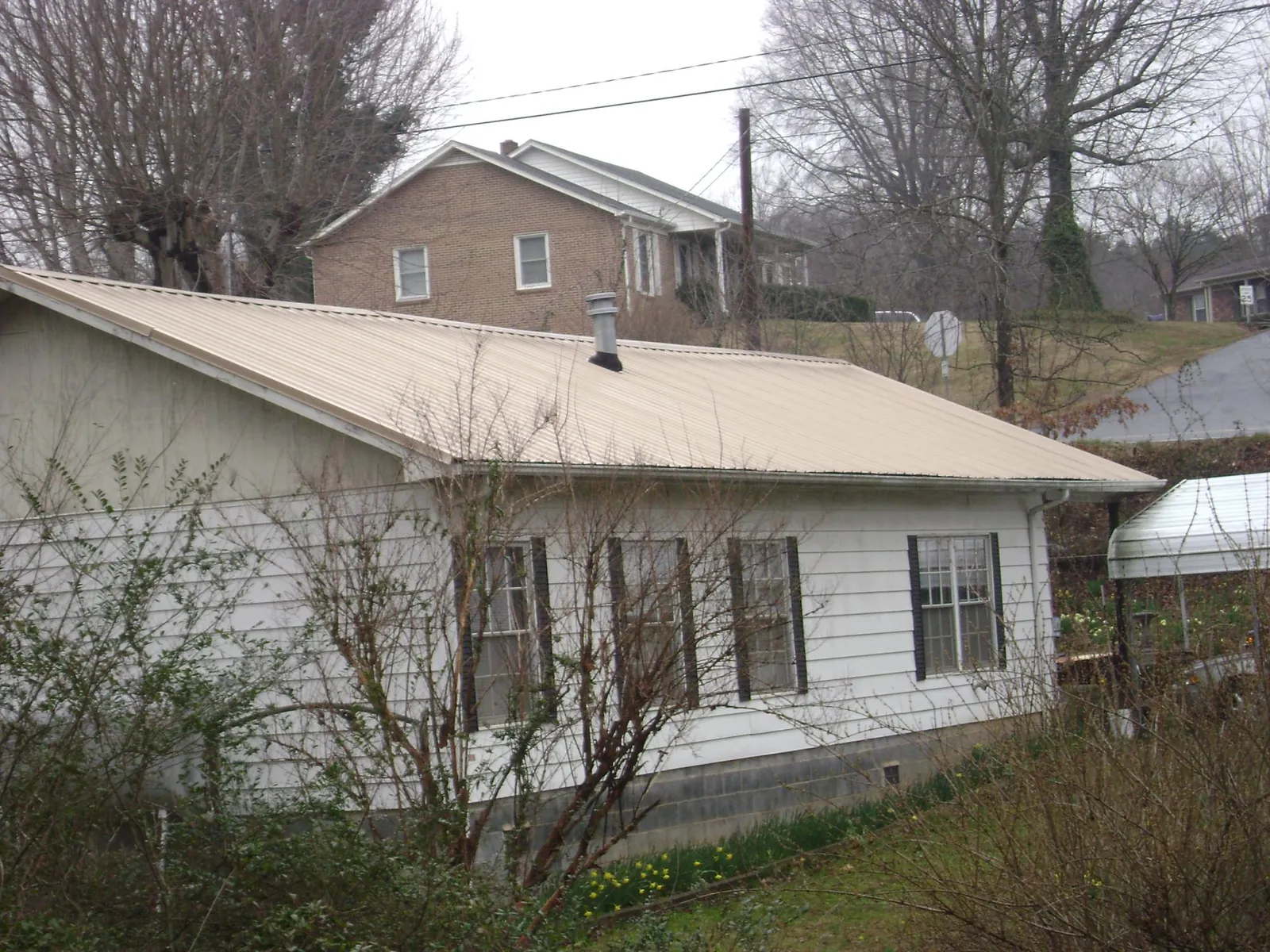 Tan metal roof on a white sided house set into a hillside — Commercial Roofing by Roofing Brothers in Carleton